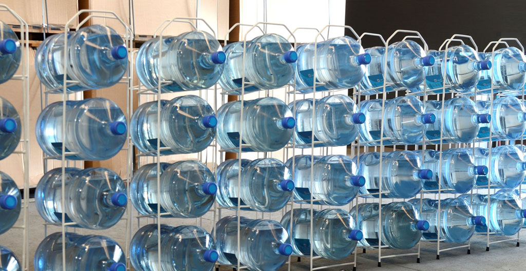 Espace de stockage professionnel avec bonbonnes d'eau organisées et livreur gérant l'approvisionnement